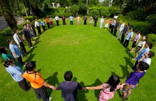 A full circle of people holding hands on open grass — the tribe